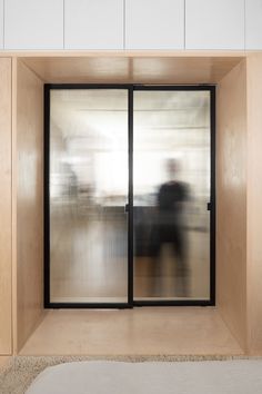 an empty room with sliding glass doors and a bed in the foreground, while a blurry person is seen through the window