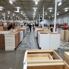 people are walking through a large warehouse with lots of unfinished cabinets in the foreground