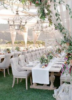 a table set up with white linens and greenery for an outdoor wedding reception