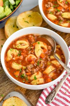 two bowls of pasta soup on a wooden table with bread and salad in the background