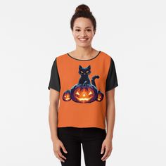 a woman wearing an orange top with a black cat on it and pumpkins in the background