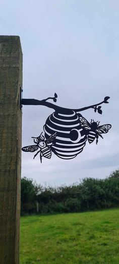 a metal insect sculpture hanging from the side of a wooden pole in front of a grassy field