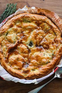 a pie sitting on top of a wooden table next to a fork and spoons