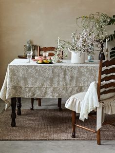 a dining room table with flowers and fruit on it, next to a chair in front of the table