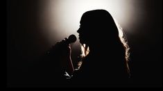 a woman with long hair holding a microphone in front of a spotlight on a dark background