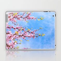 a laptop computer sitting on top of a white table next to a blue sky with pink flowers