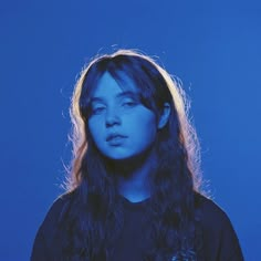 a woman with long hair standing in front of a blue background wearing a black shirt