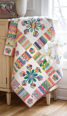 a quilted blanket sitting on top of a wooden table next to a vase with flowers