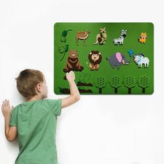 a young boy standing in front of a green board with animals on it