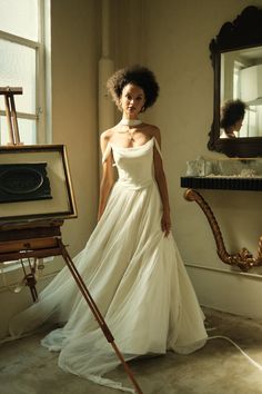 a woman in a white dress standing next to an easel