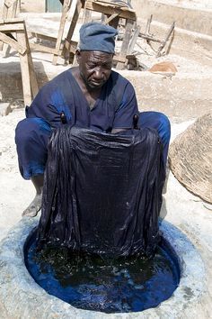 a man sitting on top of a blue pot in the middle of a cement area