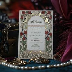 an ornate wedding card on a table next to some beads and other items in the background