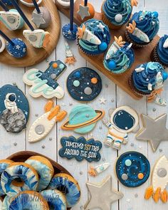 an assortment of decorated cookies and cupcakes on a white wooden table with blue decorations