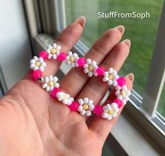 a hand holding a pink and white flower beaded heart shaped brooch on it's fingers