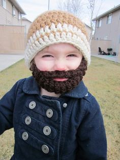 a little boy with a beard wearing a knitted hat and jacket in the grass