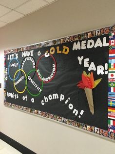 a bulletin board with the olympic rings and flowers on it in an office building hallway