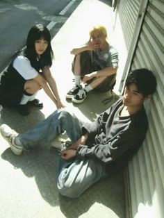 three young people sitting on the side of a building