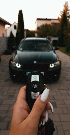 a hand holding a remote control in front of a car on a street next to another car