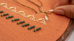 a person is working on some beading with beads and needles in front of an orange piece of fabric