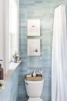 a white toilet sitting in a bathroom next to a shower curtain and framed pictures on the wall