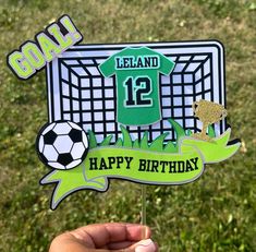 a hand holding up a soccer themed birthday cake topper that says, iceland 12 happy birthday