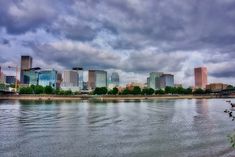 the city is surrounded by tall buildings and clouds in the sky above it, as seen from across the river