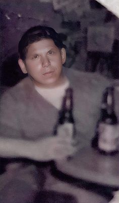 a man sitting at a table with two beer bottles in front of him and looking into the camera