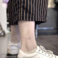 a person with a small arrow tattoo on their ankle