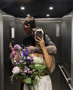 a woman taking a selfie with her phone in the bathroom while holding a bouquet of flowers