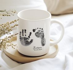 a white coffee mug with two hand prints on it sitting on top of a plate