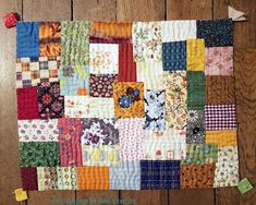 a quilt made with different colored squares on a wooden floor next to a red pom - pom