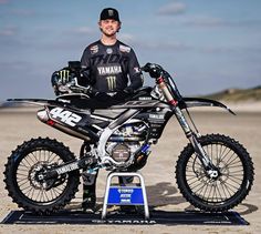 a man standing next to a dirt bike on top of a blue mat in the sand