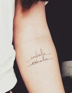 a woman with a tattoo on her arm that says, inside exhale in cursive writing