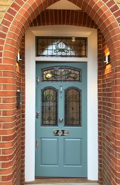 a blue front door with arched glass and brick arch on the side of a house