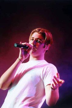 a male in a white shirt is on stage with a microphone and his hand out to the side