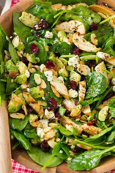 a salad with spinach, chicken and cranberries in a wooden bowl on a checkered tablecloth