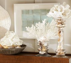 two vases filled with flowers and seashells sit on a shelf in front of a painting