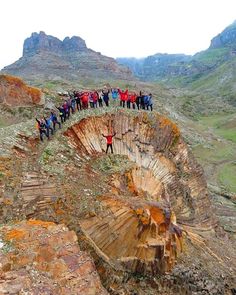 a group of people standing on the edge of a cliff with mountains in the background