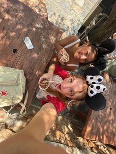 two girls are posing for the camera with mickey mouse ears on their heads and one girl is eating cereal