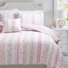 a bed with pink and white bedspread, pillows and pillow cases on it