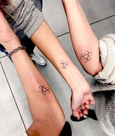 two people with matching tattoos on their legs holding hands and looking down at the ground