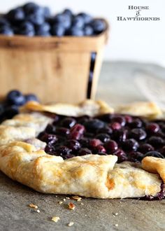 a blueberry pie sitting on top of a table next to a basket of blueberries