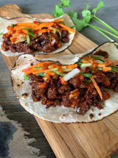 two tacos filled with meat and vegetables on a cutting board