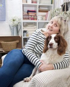 a woman sitting in a chair with her dog on her lap and she is smiling at the camera