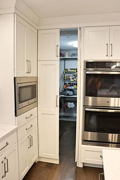 a kitchen with white cabinets and stainless steel ovens in the center, along with an open pantry door