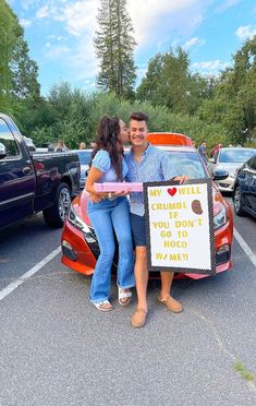 a man and woman standing next to a car with a sign in front of them