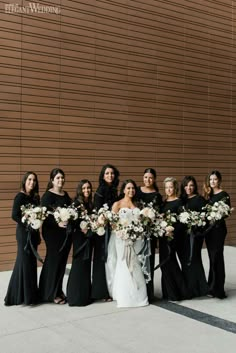 a group of women standing next to each other in front of a wall holding bouquets