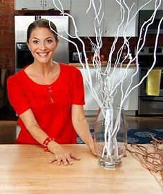 a woman standing in front of a wooden table with vases and branches on it