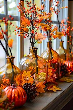 some glass vases filled with plants and autumn leaves on a window sill in front of a window