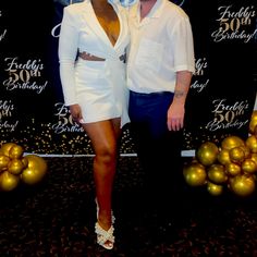 a man and woman standing next to each other in front of a backdrop with balloons